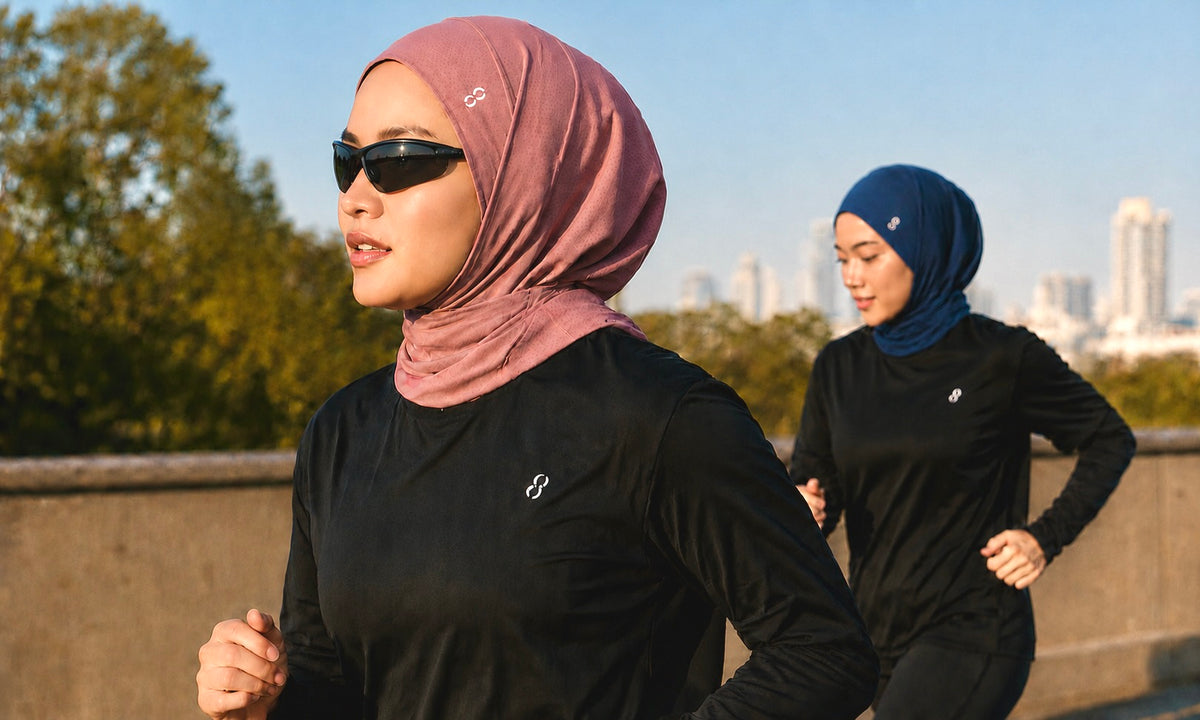 Two women jogging outdoors in matching black athletic long-sleeve tops and hijabs, one in dusty pink and one in navy blue, with trees and a city skyline in the background.