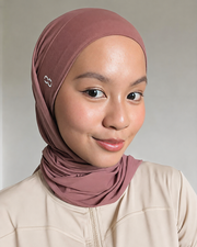 A woman wearing a dusty rose hijab and a beige zip-up jacket, photographed against a neutral light gray background.